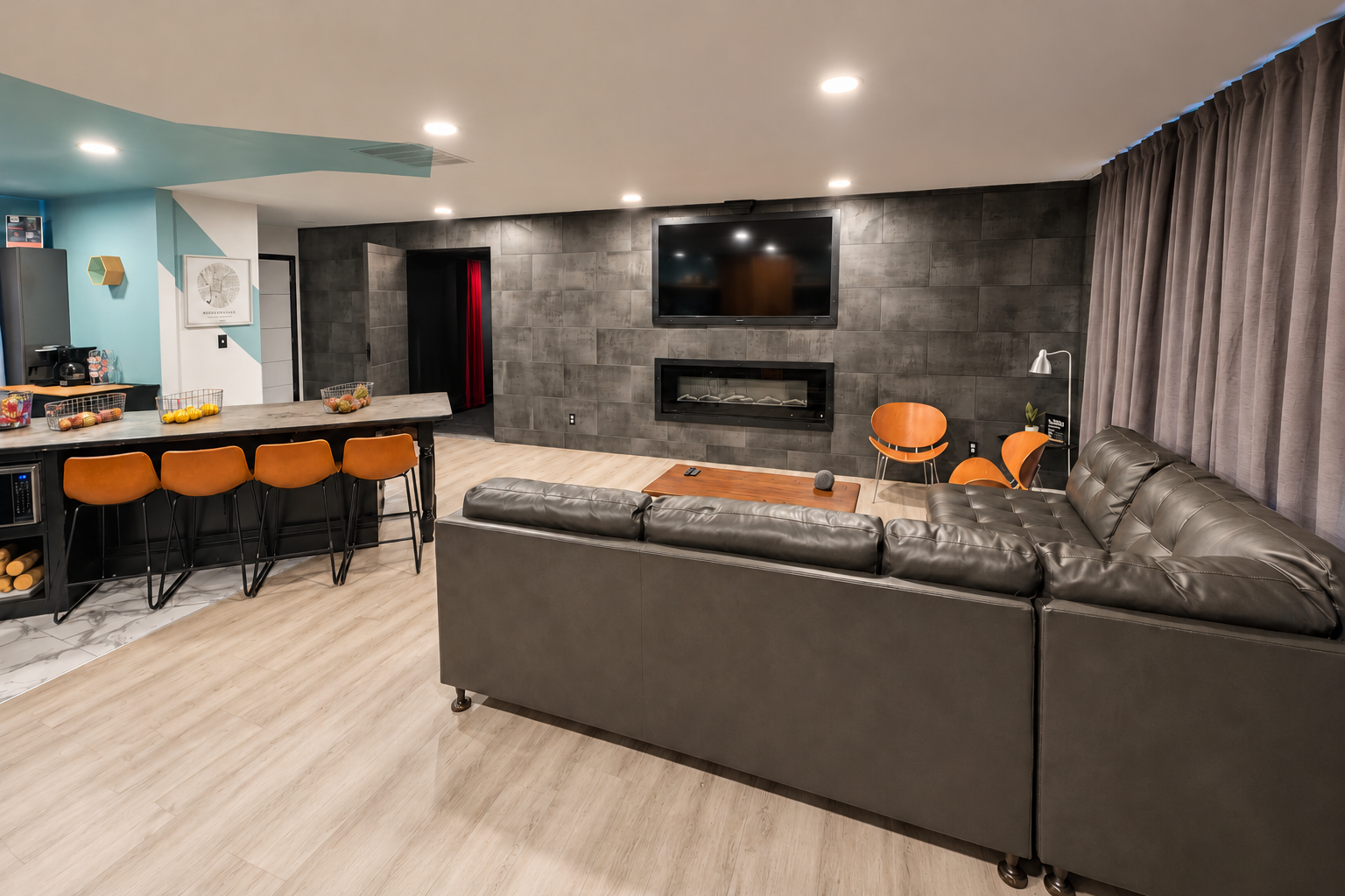 Furnished living room with large wall-mounted TV, modern fireplace, comfortable seating and kitchen island